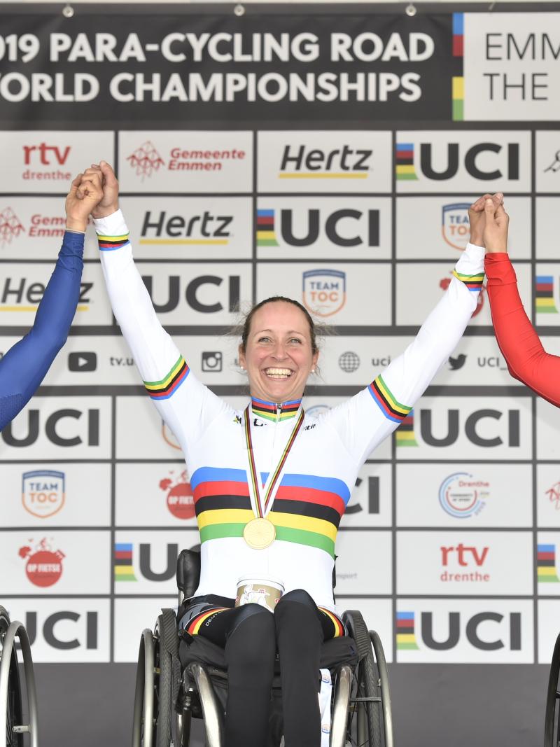 Three wheelchair cyclists hold hands on podium