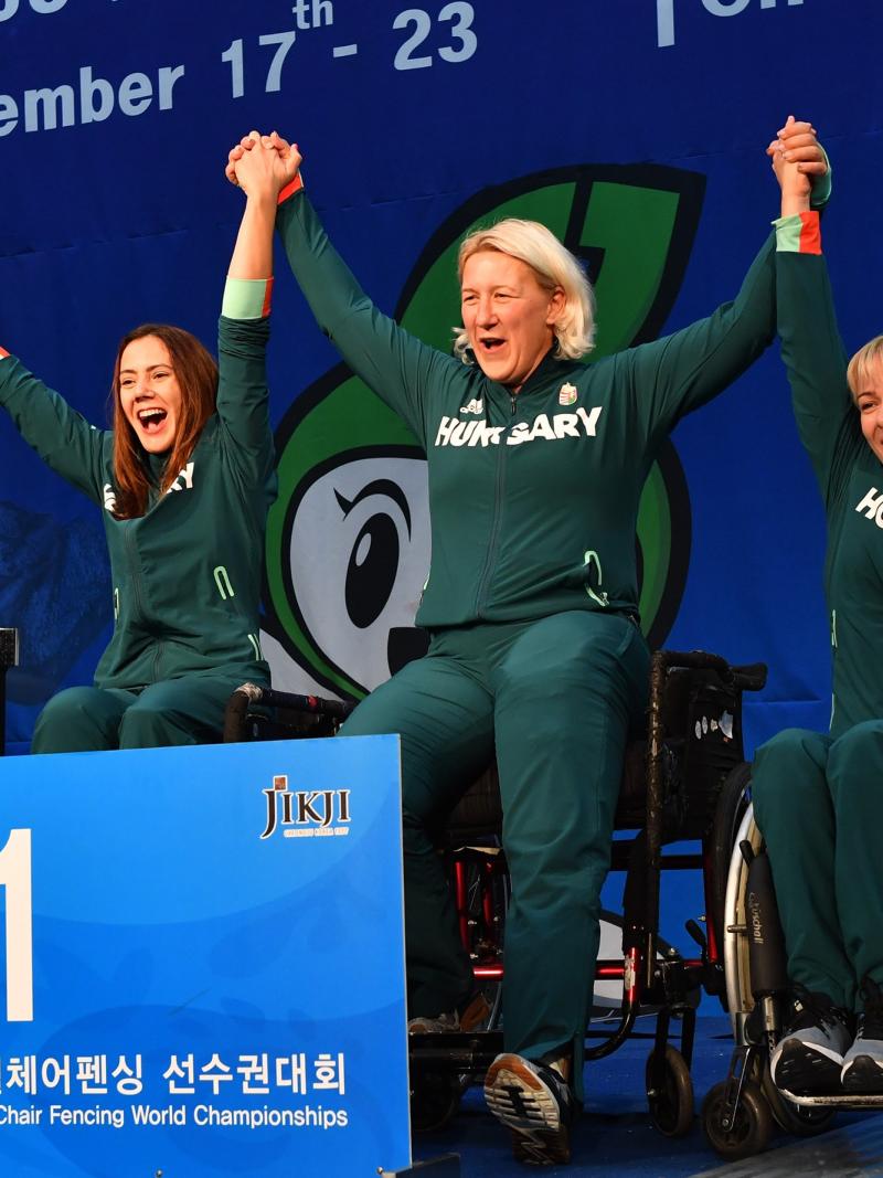 Four Hungarian female wheelchair fencers hold hands on the podium