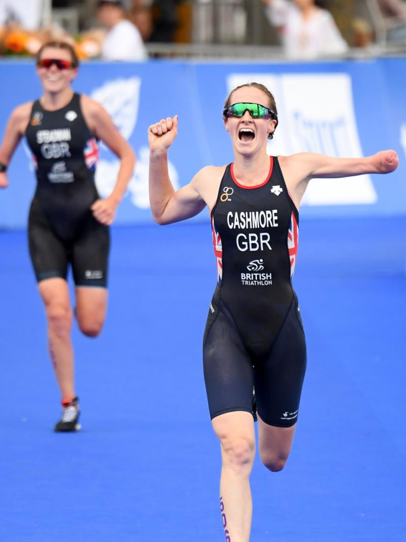 Female triathlete with arm amputation celebrates with opponent in background smiling