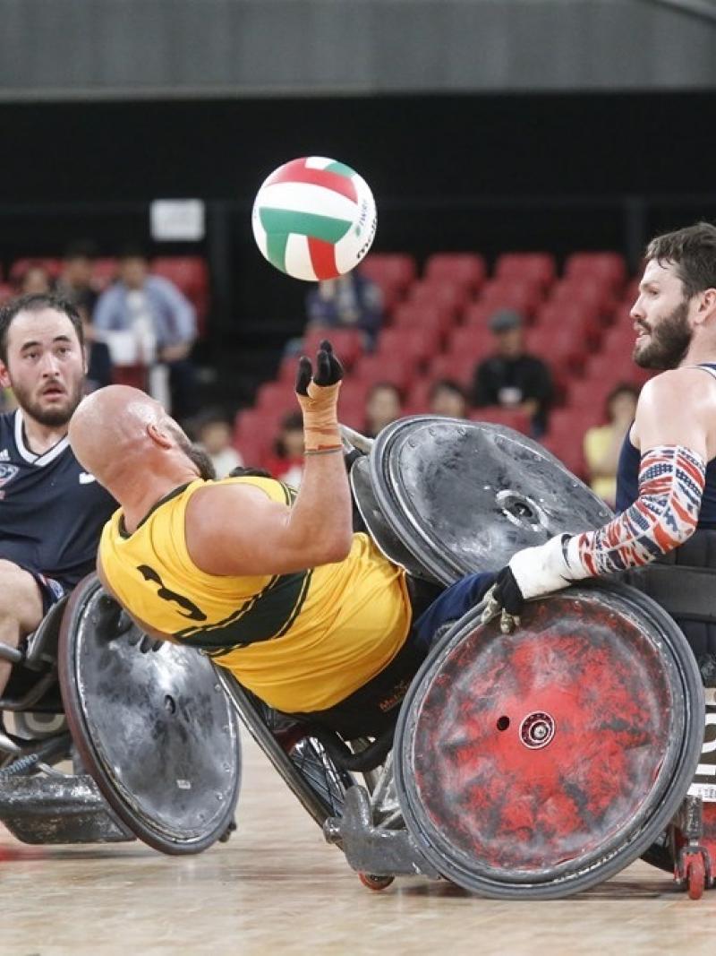 Two wheelchair rugby players knock over an opponent