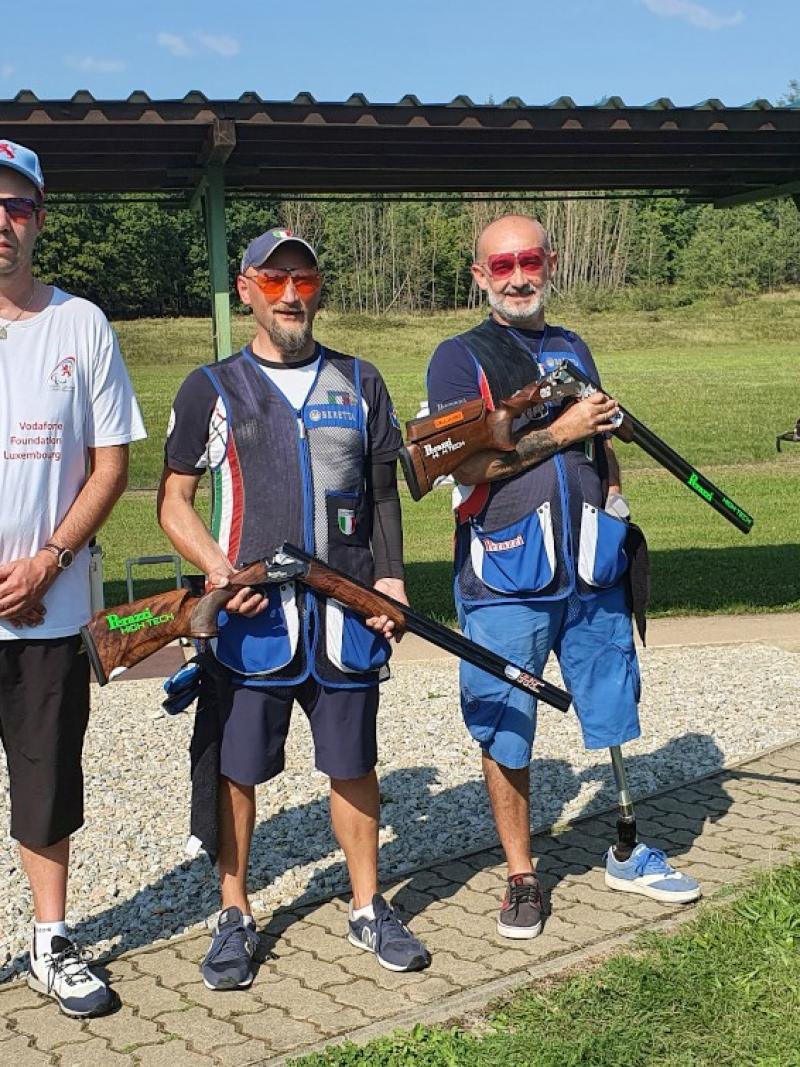 Three men standing on a shooting range, two of the holding shotguns 