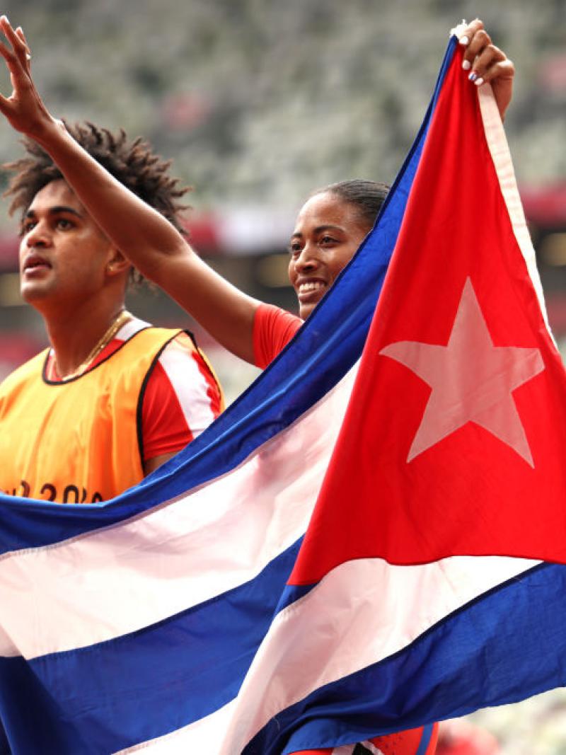 A male and a female sprinter holding the flag of Cuba in an athletics stadium