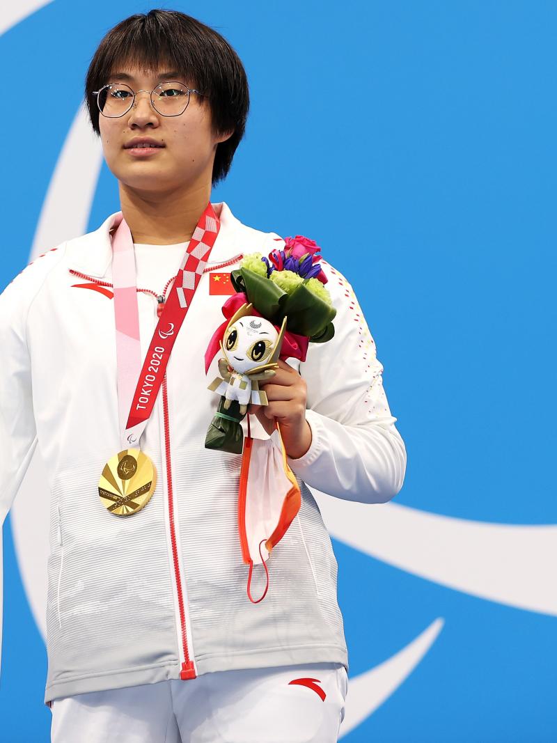 A woman poses with a gold medal, holding the mascot in her left hand