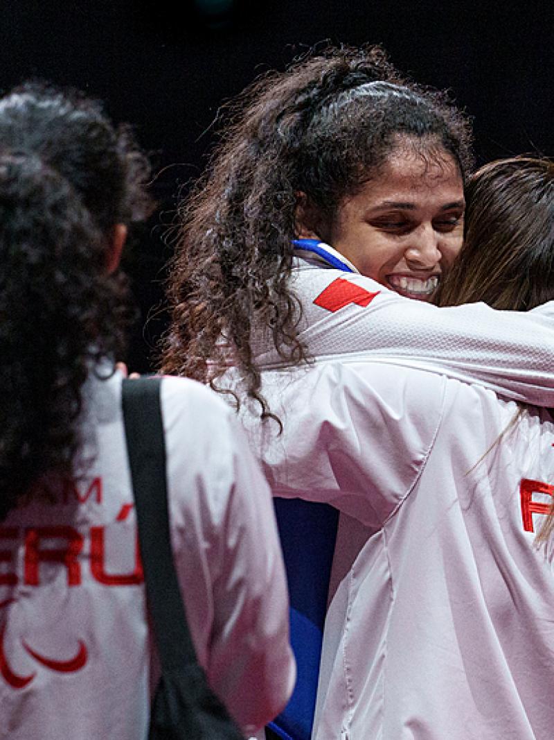 Leonor Espinoza Carranza smiles and hugs a colleague wearing a white jacker with peru on the back