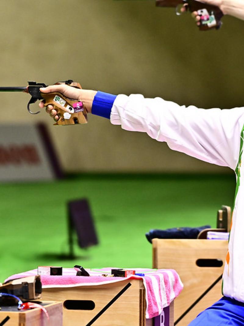 A man with a hat competing in a pistol shooting event in a shooting range