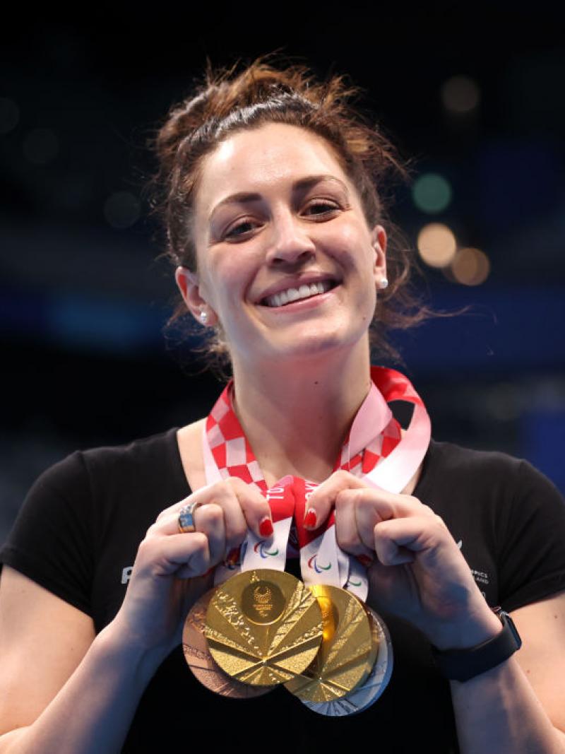 A Para swimmer posing with four medals and smiling to the camera