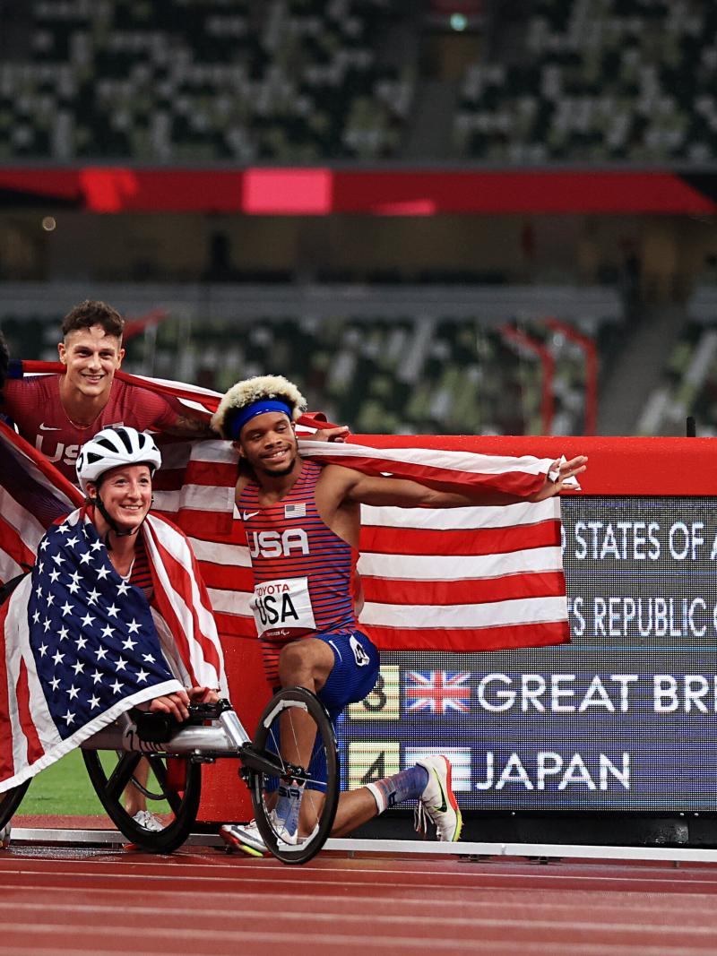 Four athletes celebrating with flags in front ofthe results screen