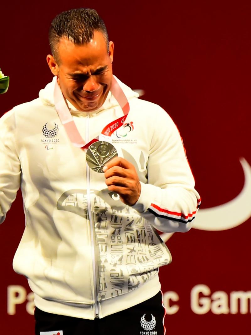 A man crying and holding a silver medal in his left hand with a mascot in his right hand.