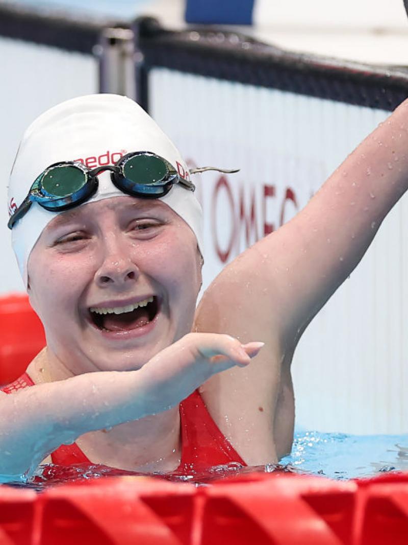A Para swimmer hanging onto the edge of the pool with a smile on her face