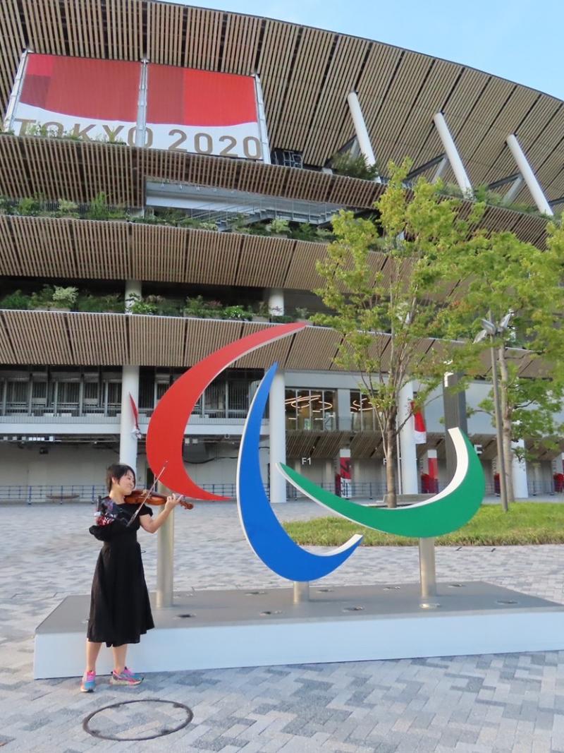 A former Paralympian poses with a violin in front of the Agitos symbol at the Olympic Stadium in Tokyo.