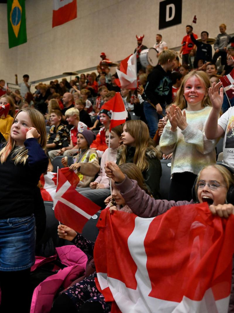 Children holding Denmark's flags fill the stands at a venue