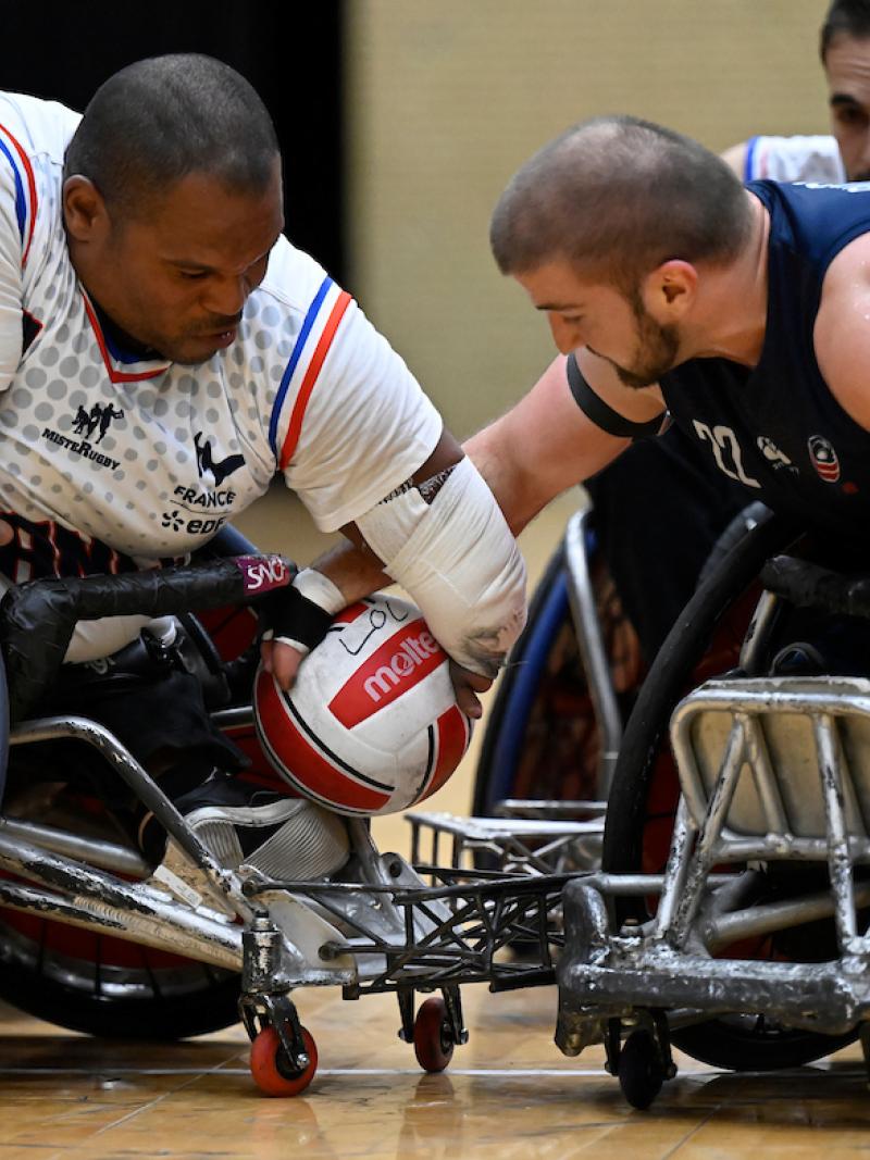 Two wheelchair rugby players reach for a ball