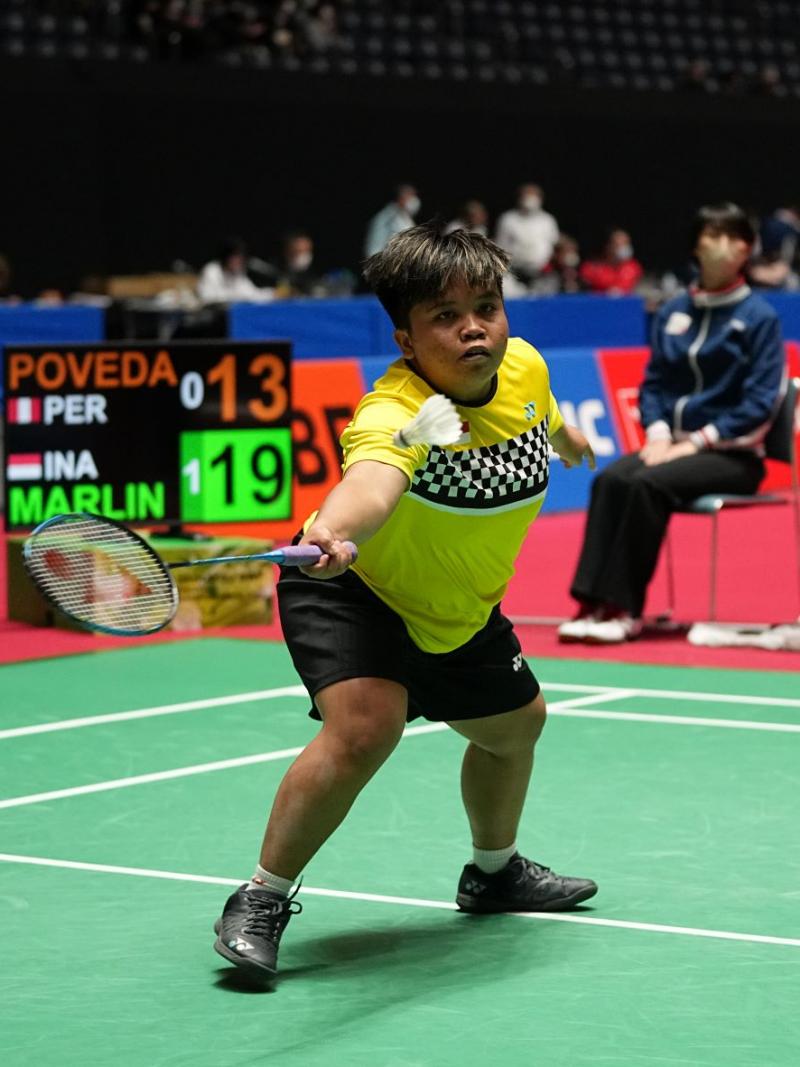 A female athlete holds a racket with her left hand and reaches out for the shuttle.