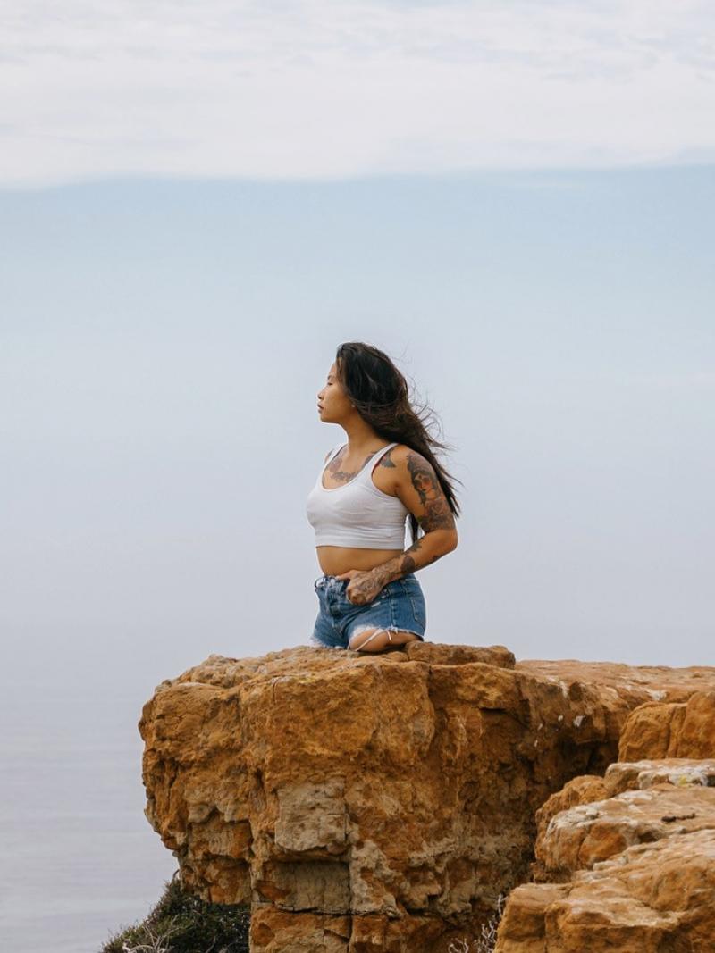 A young female without legs below the hips stands on a cliff looking out a large body of water.