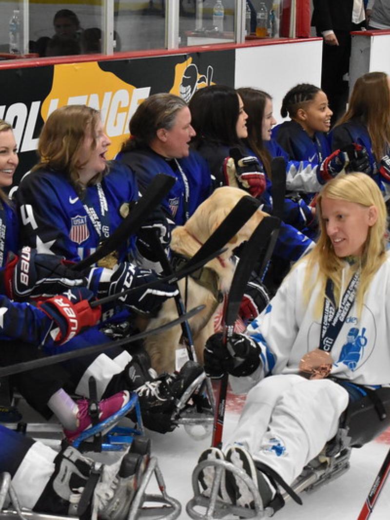 Female athletes in blue jersey are on the ice, while a female athlete in white jersey passes by.