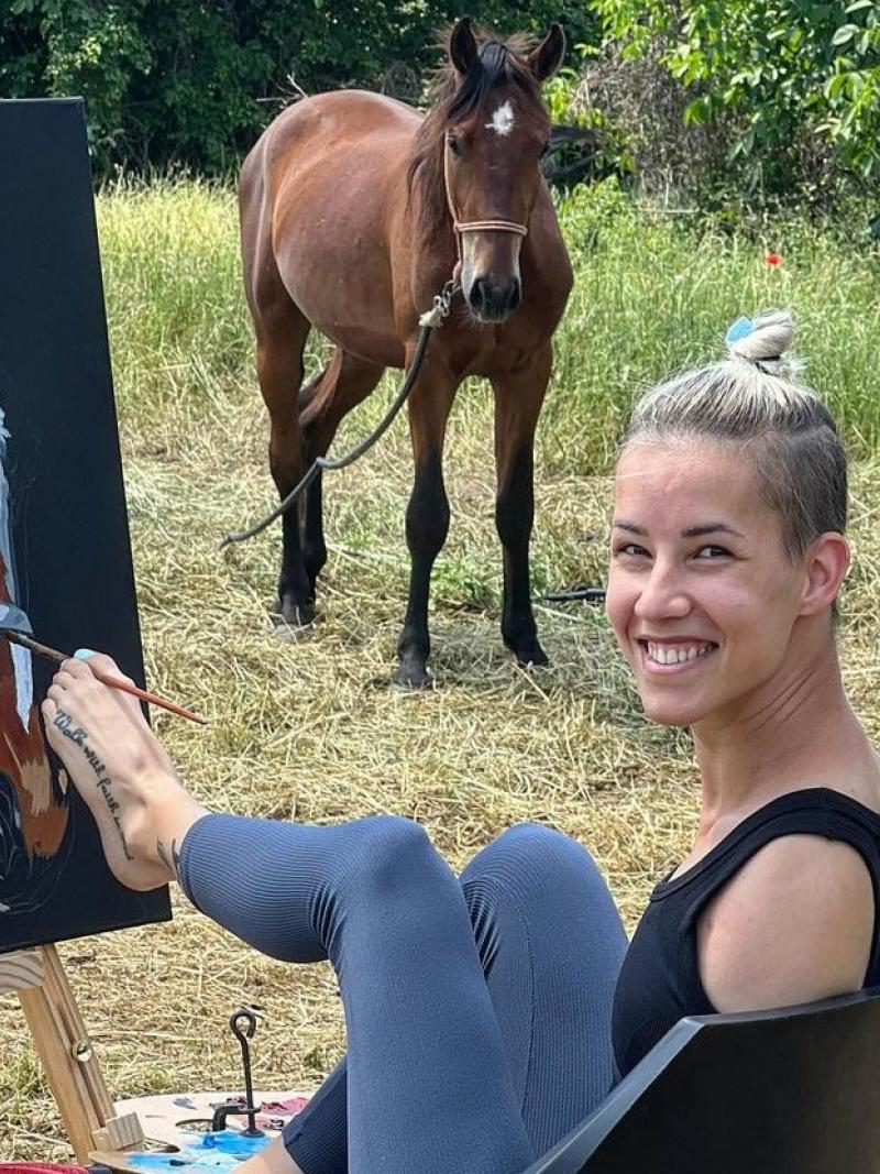 A female paints a picture of a horse with her left foot.