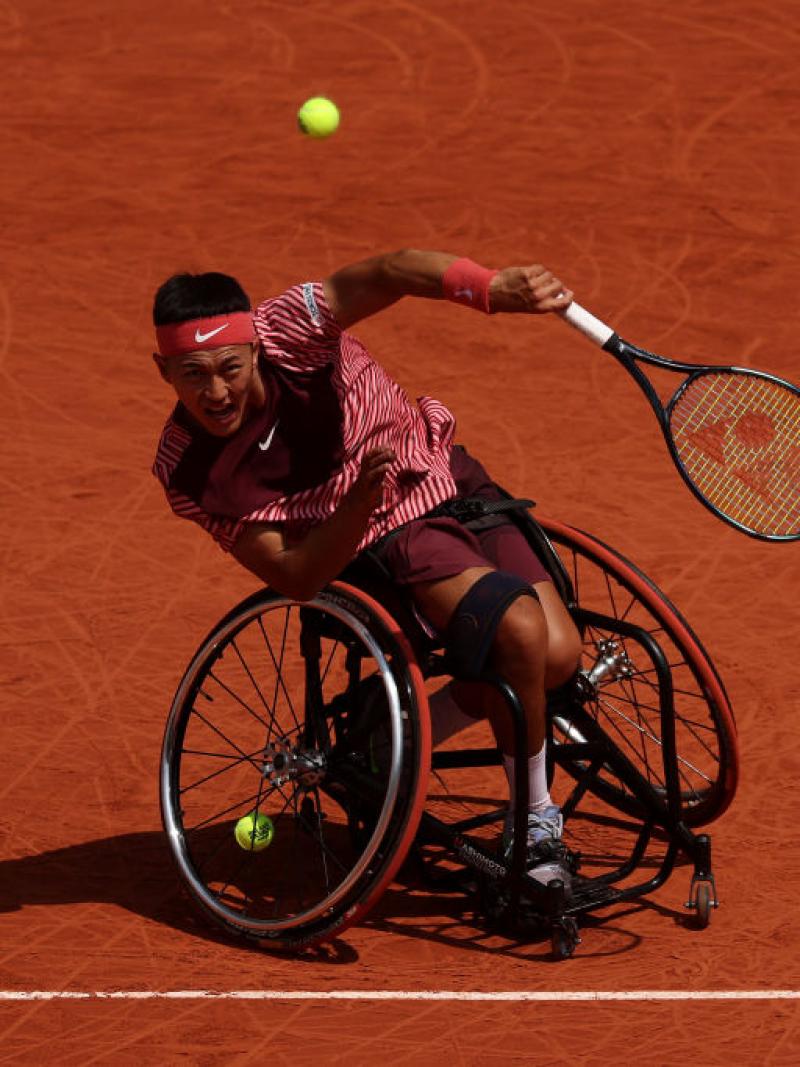 A male wheelchair tennis player swings his racquet during competition.