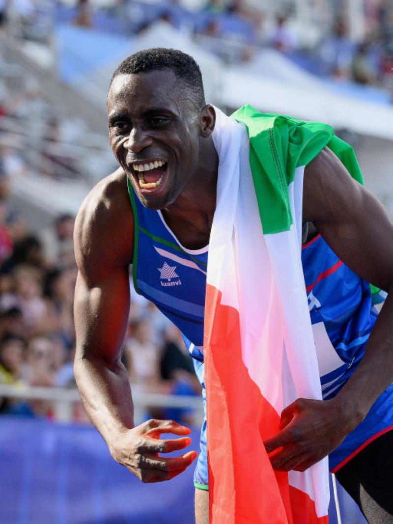 A man in athletics outfit celebrating with the Italian flag