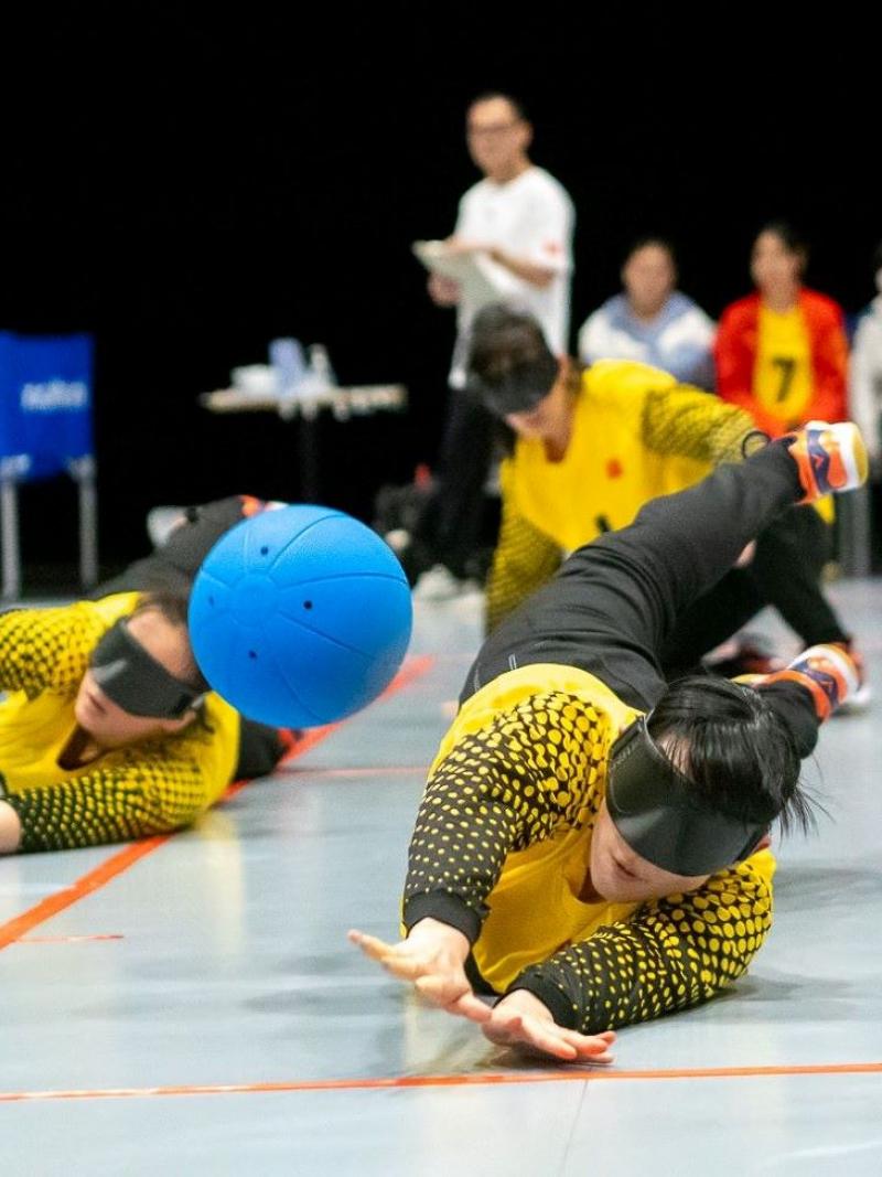 Two female athletes block a blue ball during a goalball match