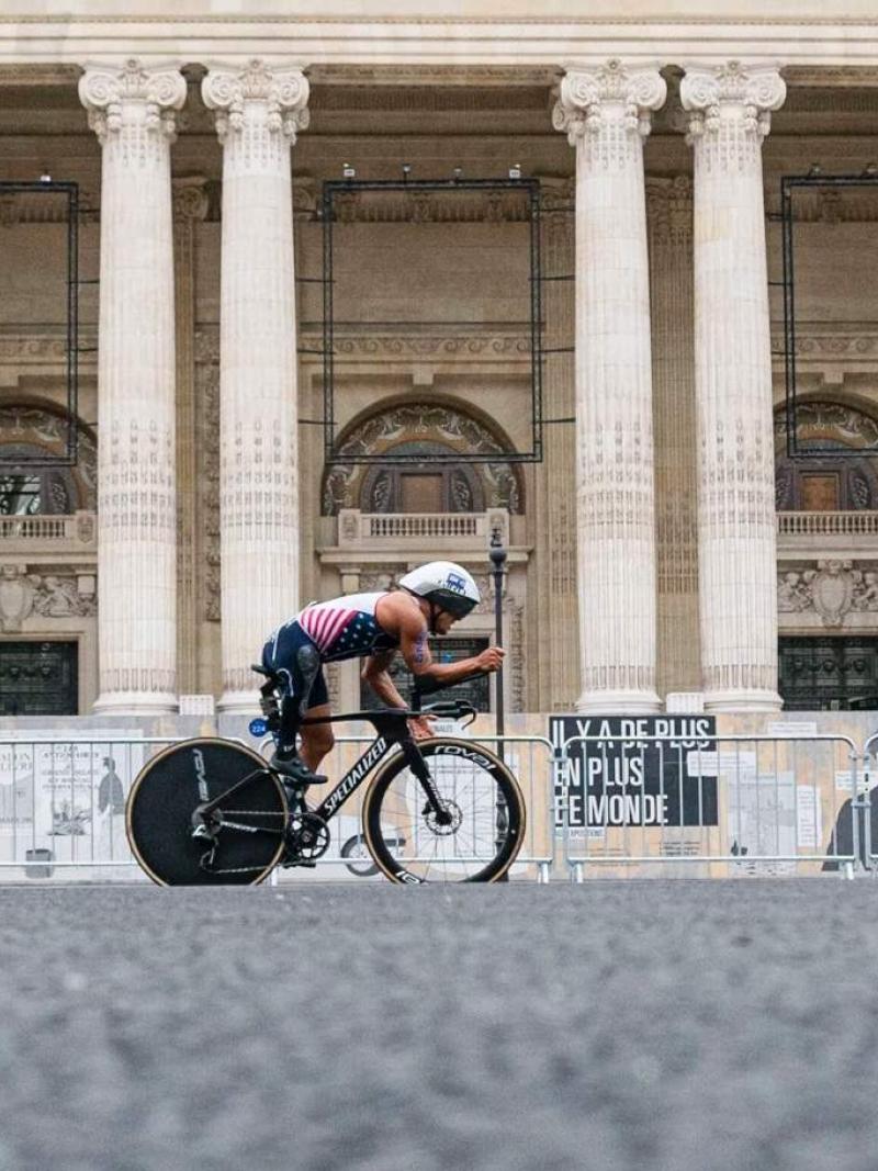 A Para triathlete on a bike cycles past a Parisian monument