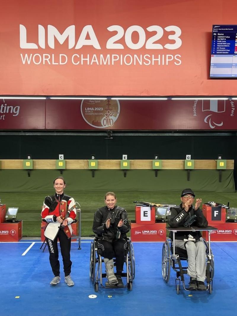 A standing woman next to a woman and a man in wheelchairs in a shooting range