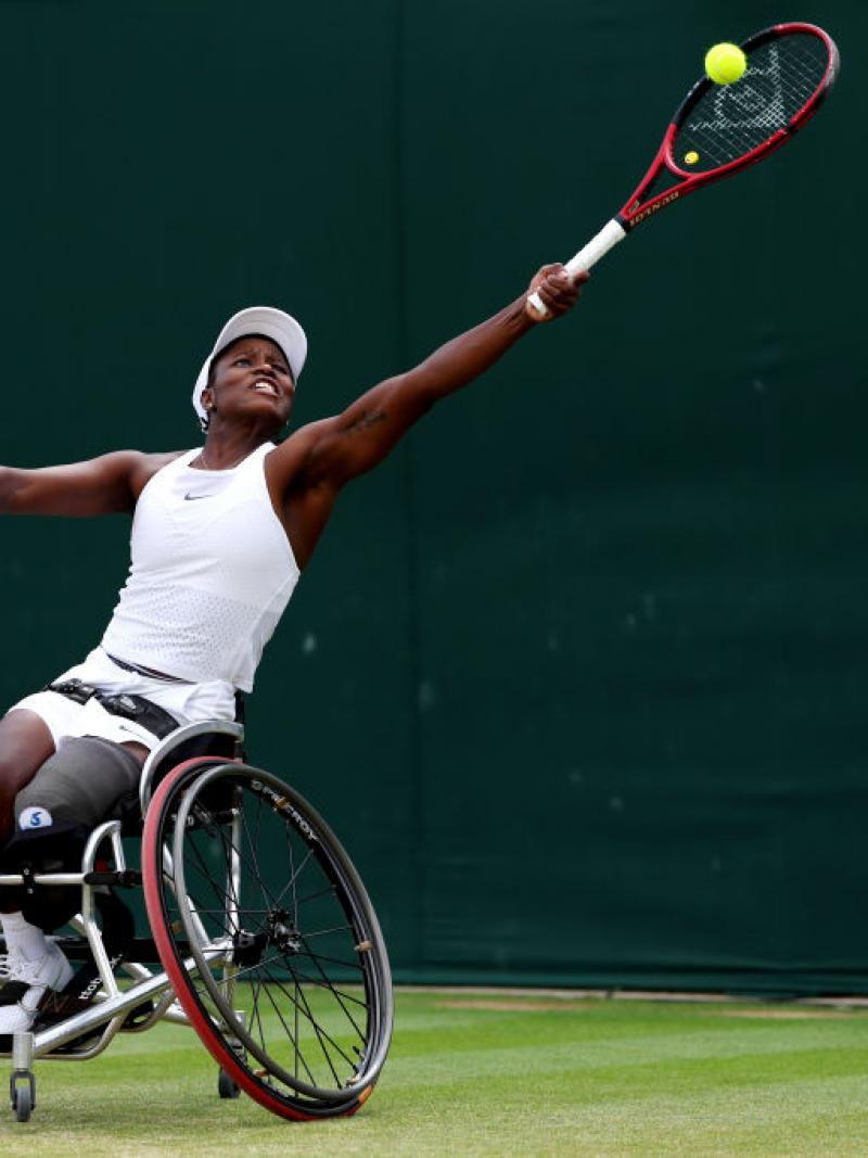 A female wheelchair tennis player stretches to play a forehand during a match.