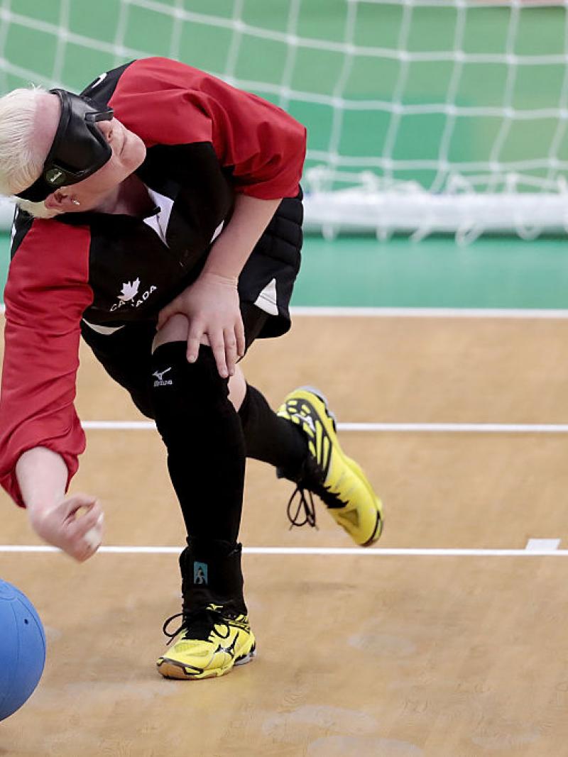 A female athlete throws a blue ball in front of the net during a goalball game. 