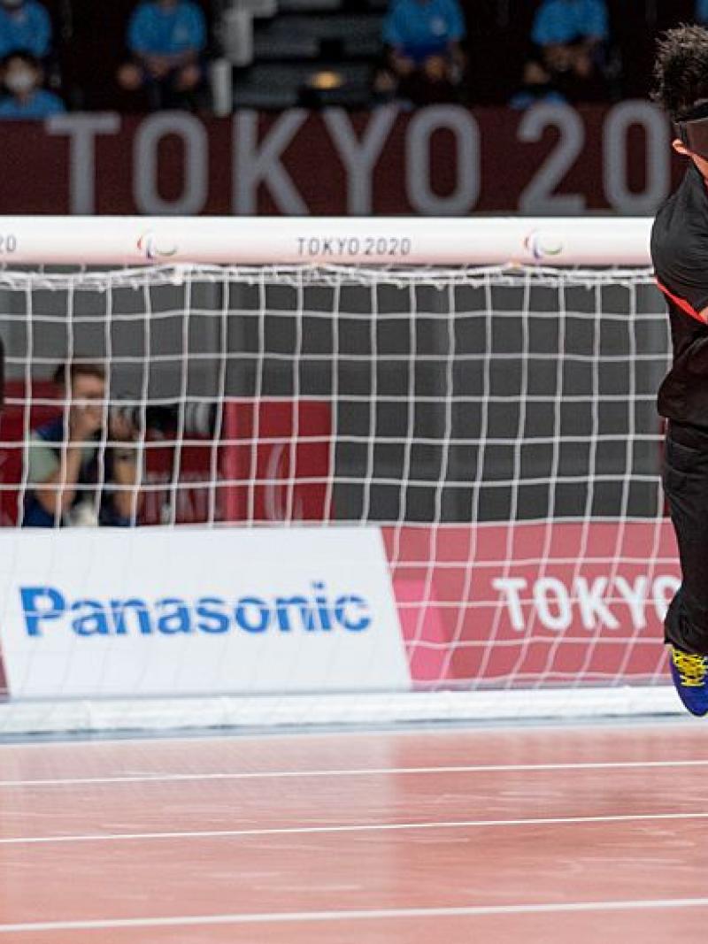 A male goalball player rolls the blue goalball in front of his net.