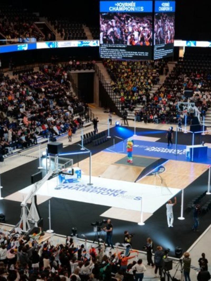 A wide shot of a basketball court. Many people are in the stands