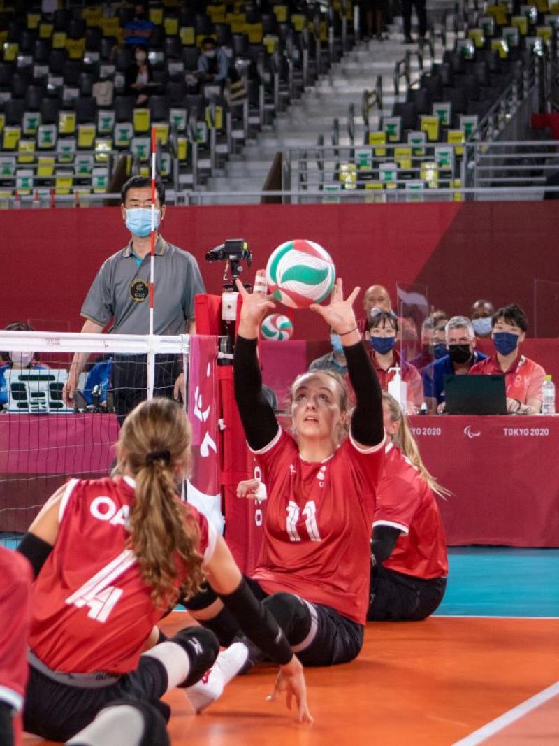 A female sitting volleyball athlete sets the ball during competition