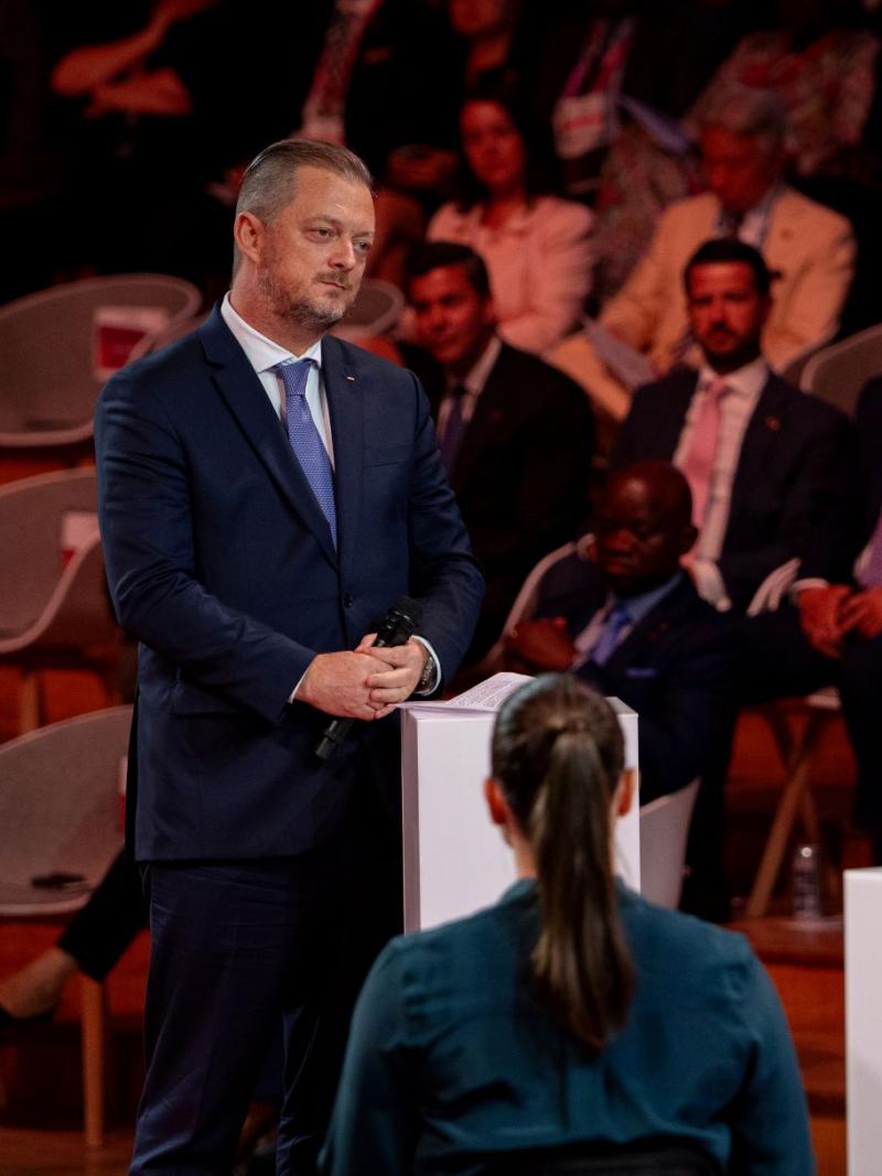 Andrew Parsons, IPC President, stands on the stage with two participants. People 