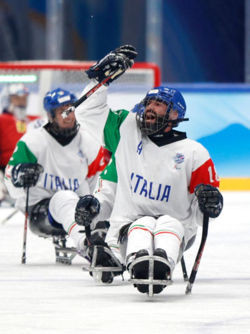 A male Para ice hockey player celebrates by raising his Para ice hockey stick on the ice