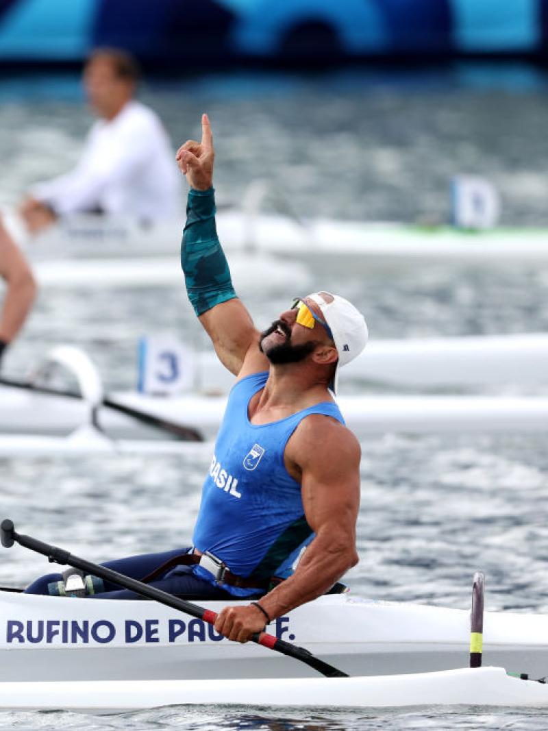 A male Para canoe athlete celebrates after winning his race - he is pointing his right index finger to the sky.