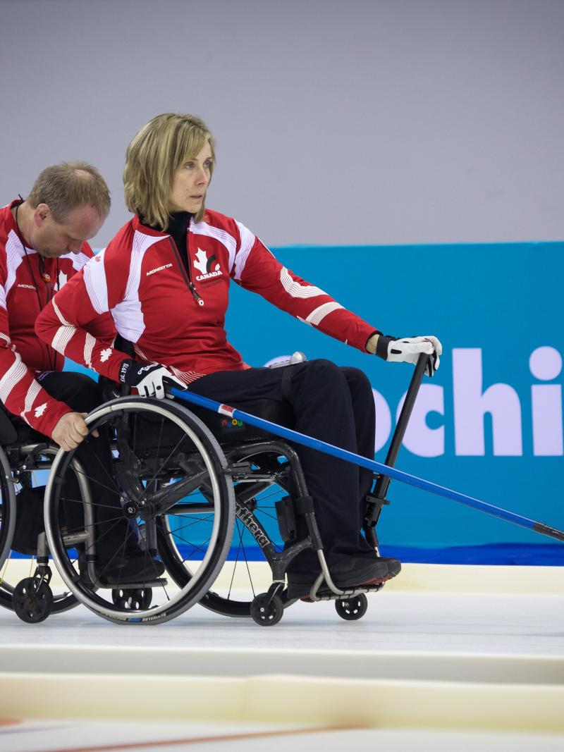 A picture of 2 person in wheelchairs playing curling
