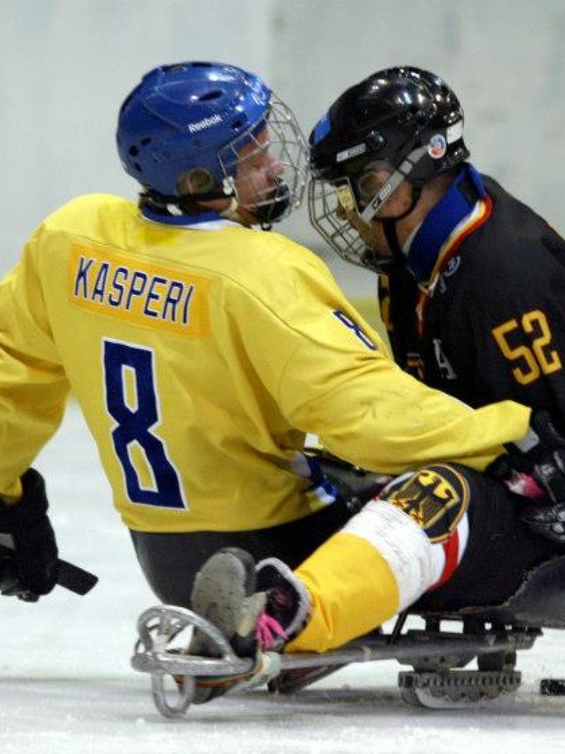 A picture of 2 men in sledges playing ice hockey