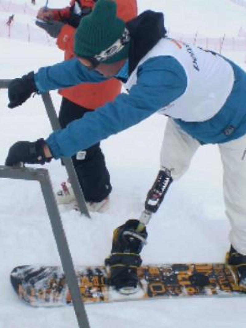 A picture of a man with a prosthesis practising snowboard