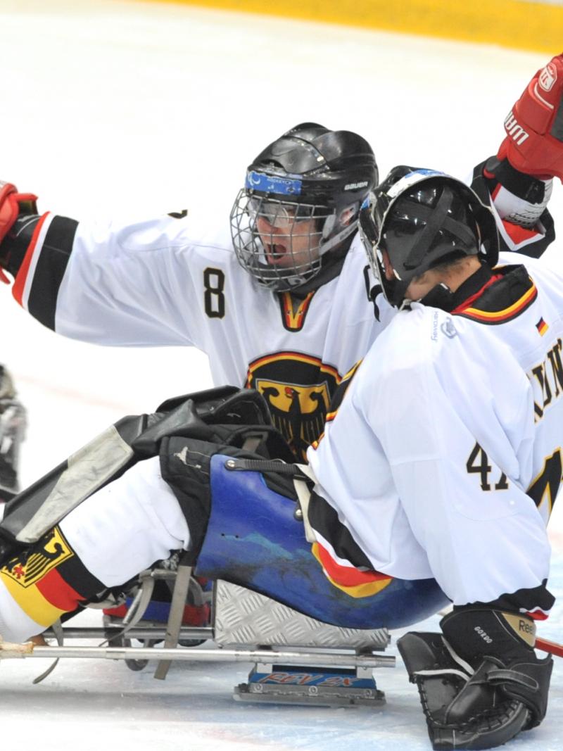A picture of 2 men in sledges celebrating a goal during a ice sledge hockey match