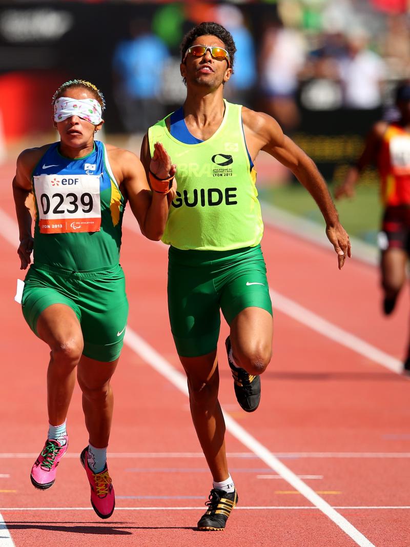A visually impaired athlete runs with her guide on the track of a stadium.