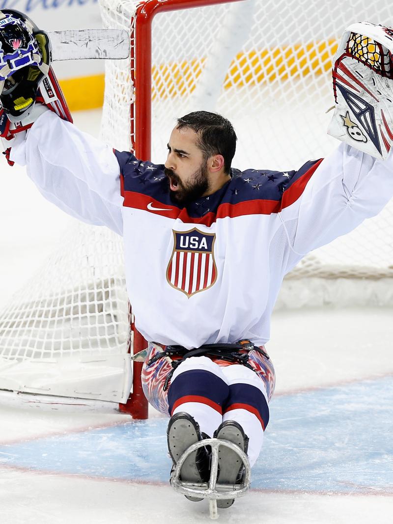 An ice sledge hockey goaltender raises his arms in celebration.