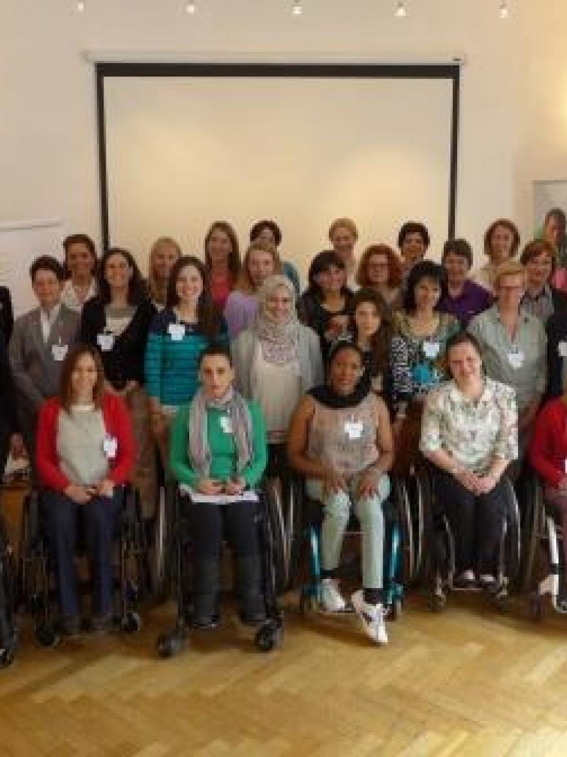 Group shot of women (standing and in wheelchairs) in front of a white wall.