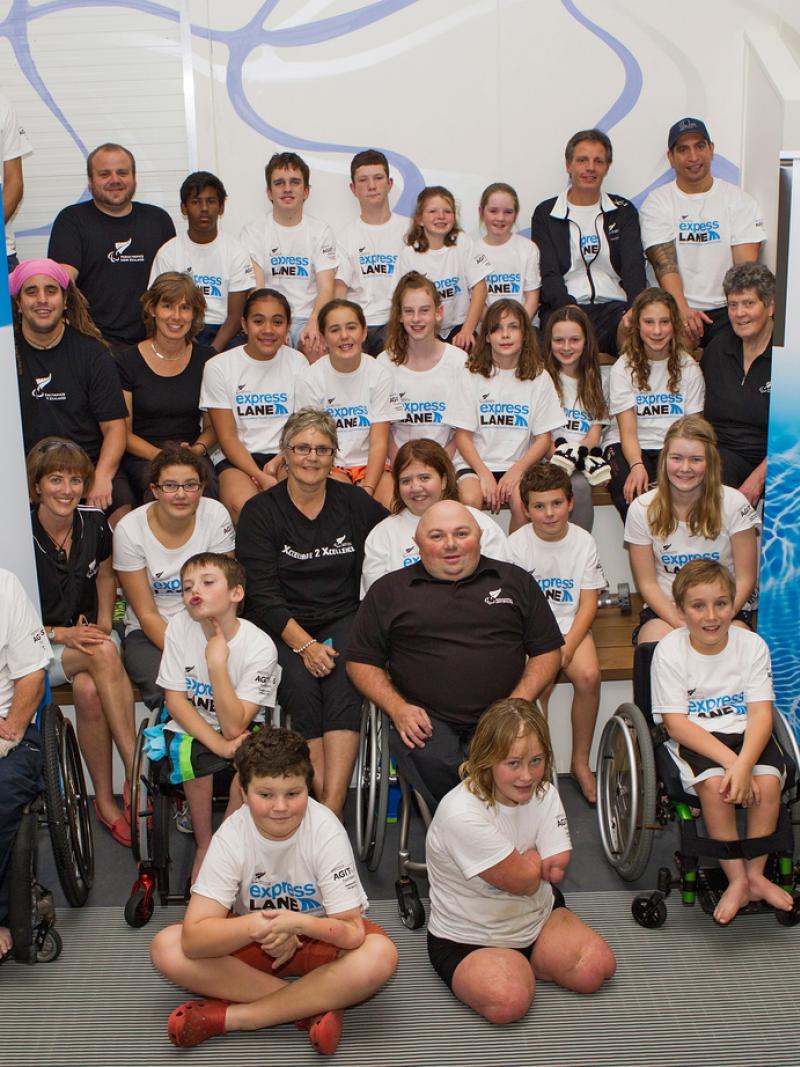 A group of participants pose in front of Paralympics New Zealand and Agitos Foundation banners.