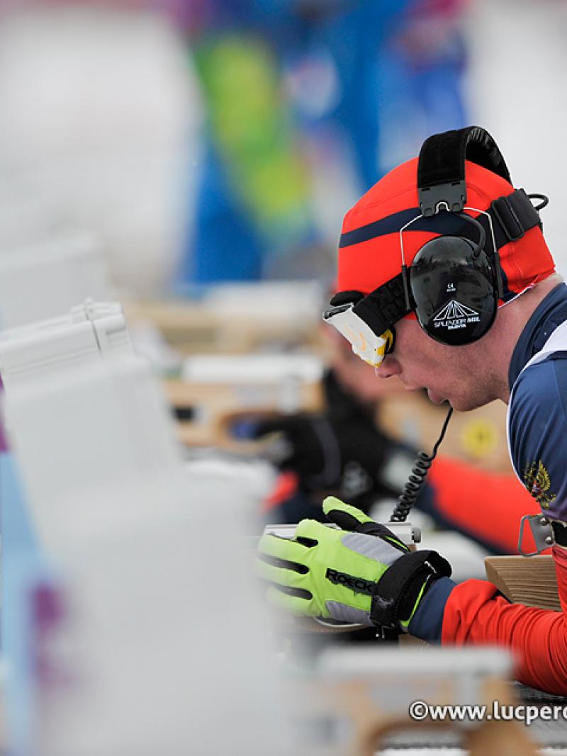 Athlete with ear phones takes aim in biathlon.