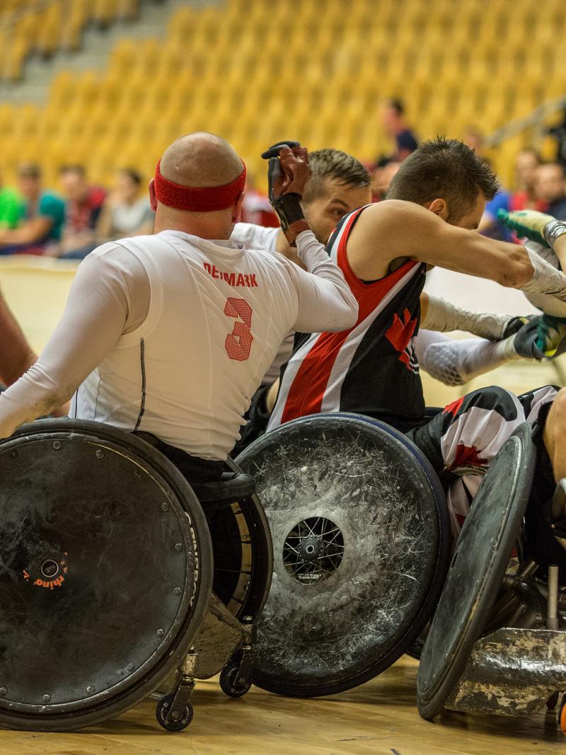 A group of four players in wheelchairs - two per side - fight for the ball during a wheelchair rugby match.