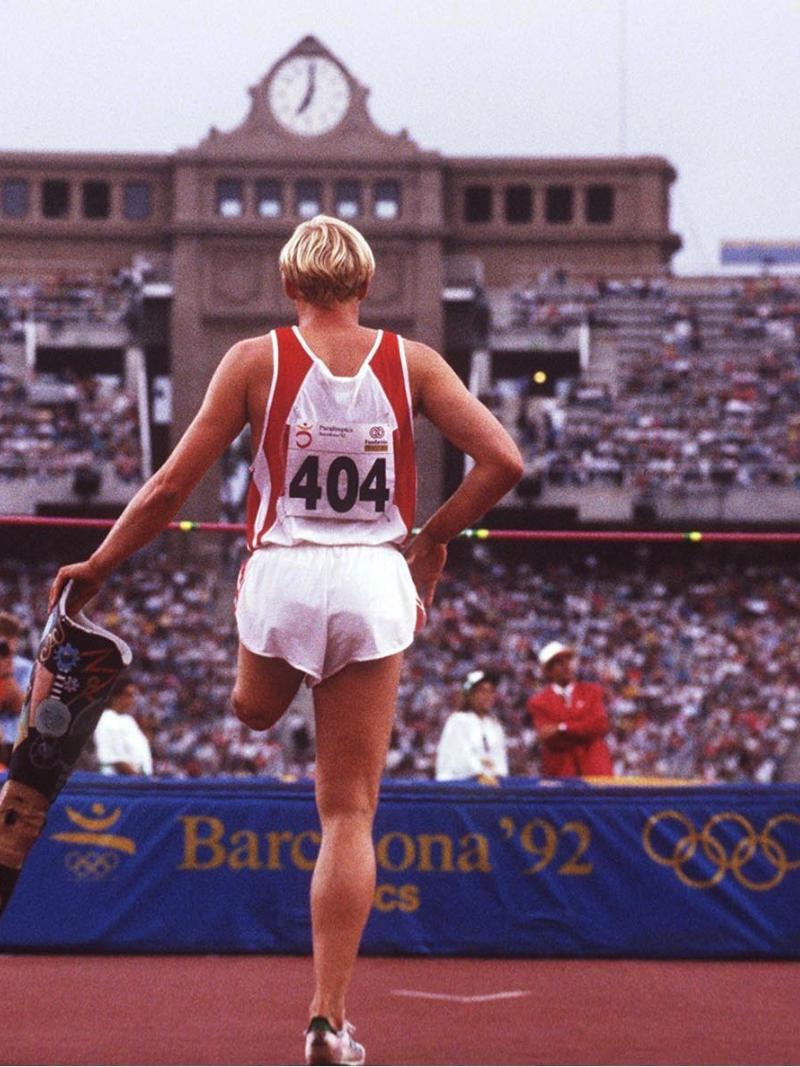 High jumper looking at the bar while holding a prosthetic leg in his hand.