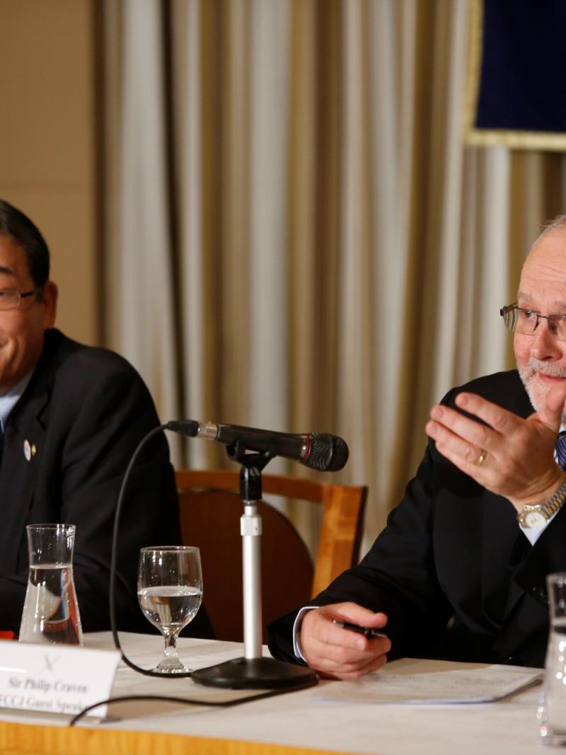 Two men sitting on a podium behind a table with microphones in front of them