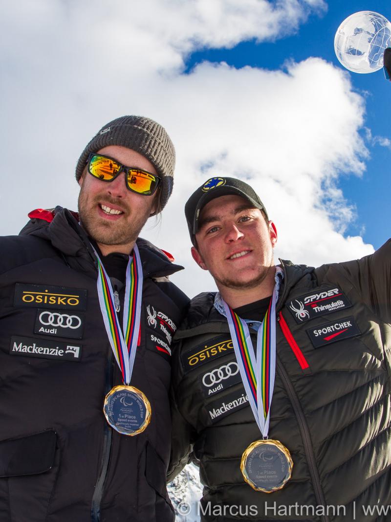 Upper bordies of two men smiling, showing their medals to the camera