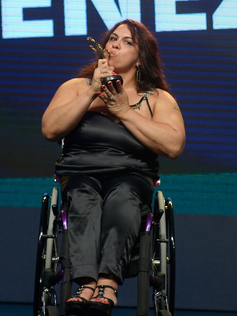 Women in black dress sitting in a wheelchair kissing a trophy