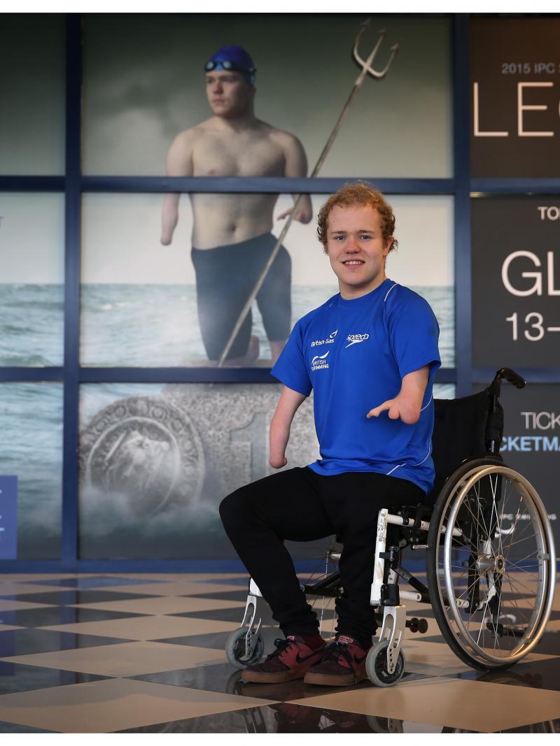 Man in wheelchair poses in front of a wallpaper