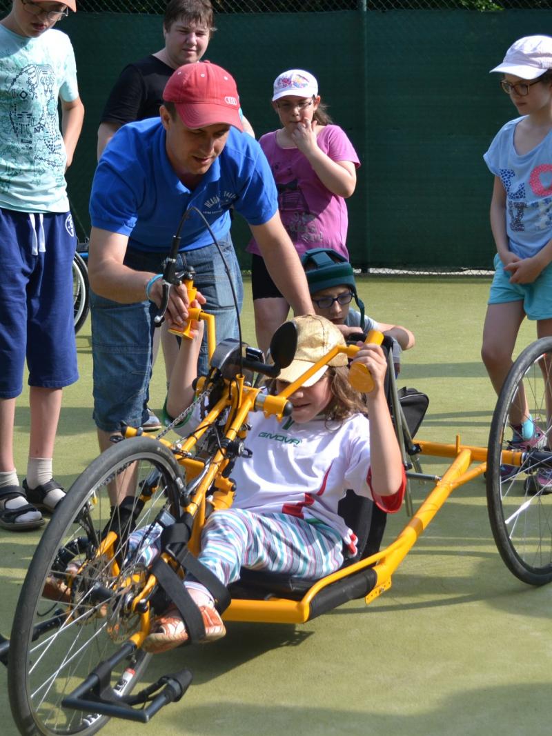 Kid in a handbike with other people standing around and watching