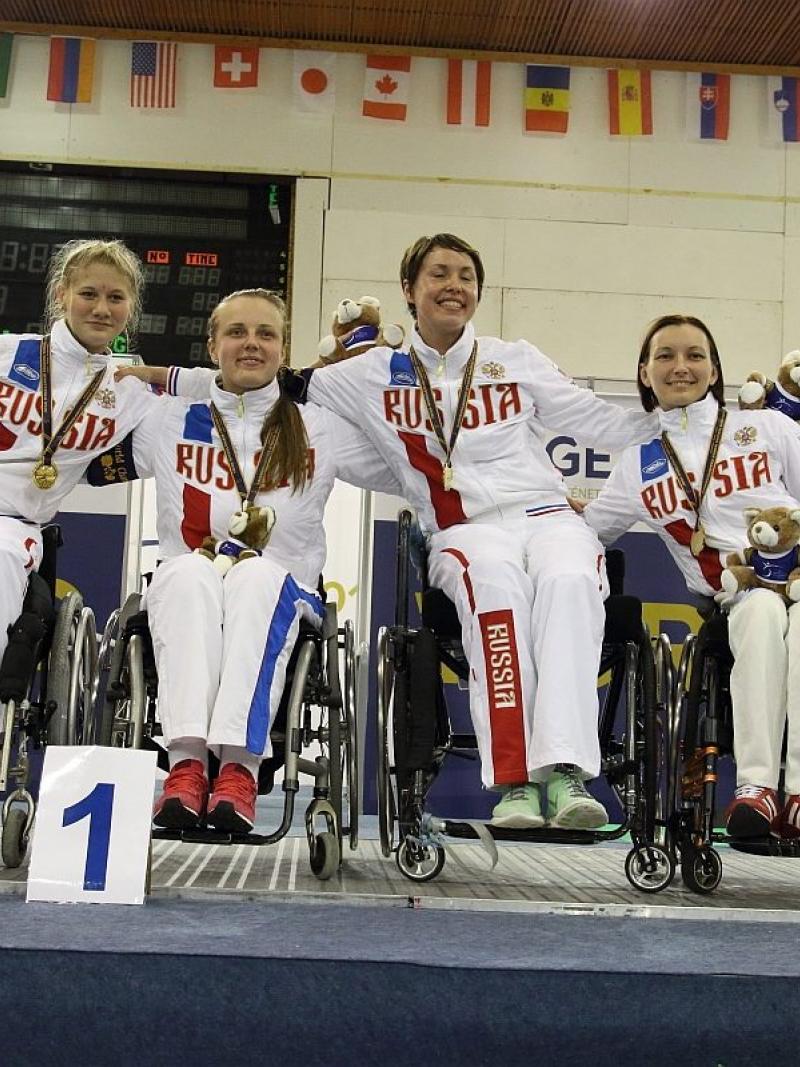 Four women in wheelchairs on a podium, posing with medals
